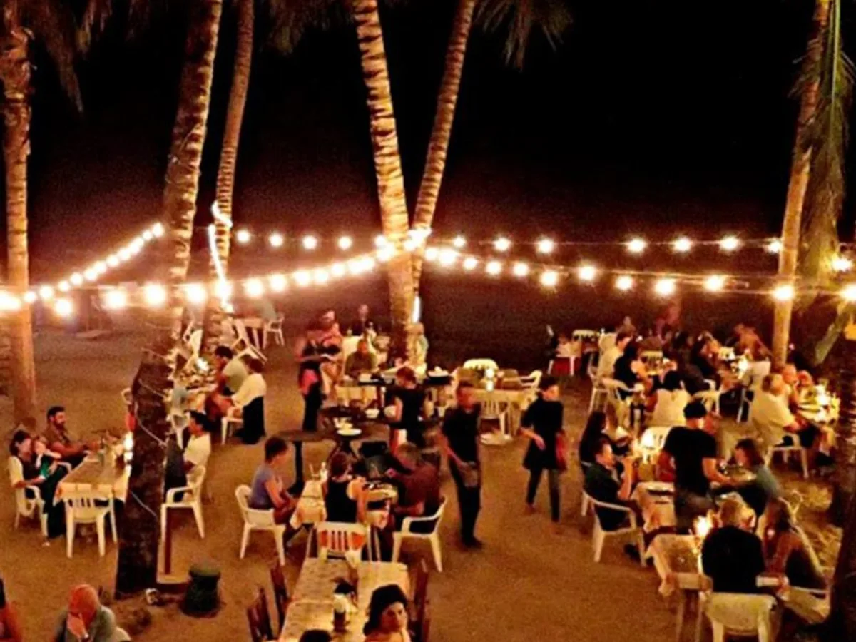 Beachfront dining tables under palm trees strung with lights at La Casita de Papi in Cabarete