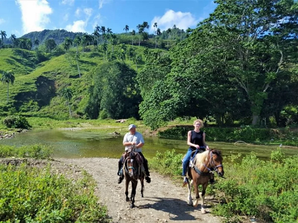 Two riders on horseback beside a river in the countryside near Cabarete