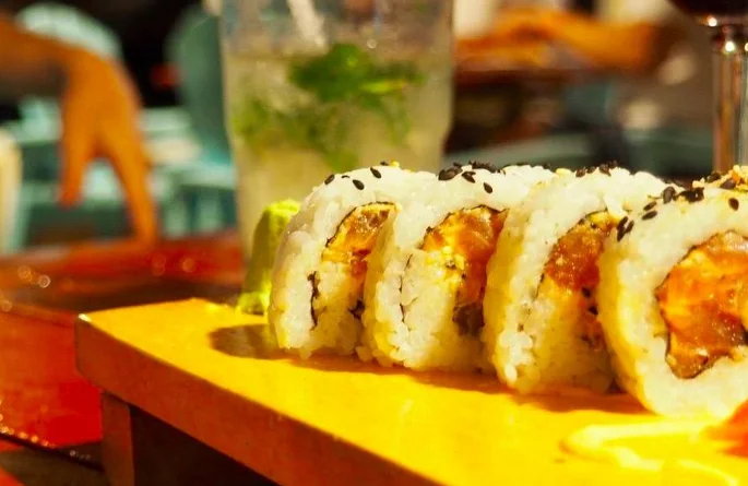 Sushi roll topped with sesame seeds, served on a wooden board at La Mesa Taína