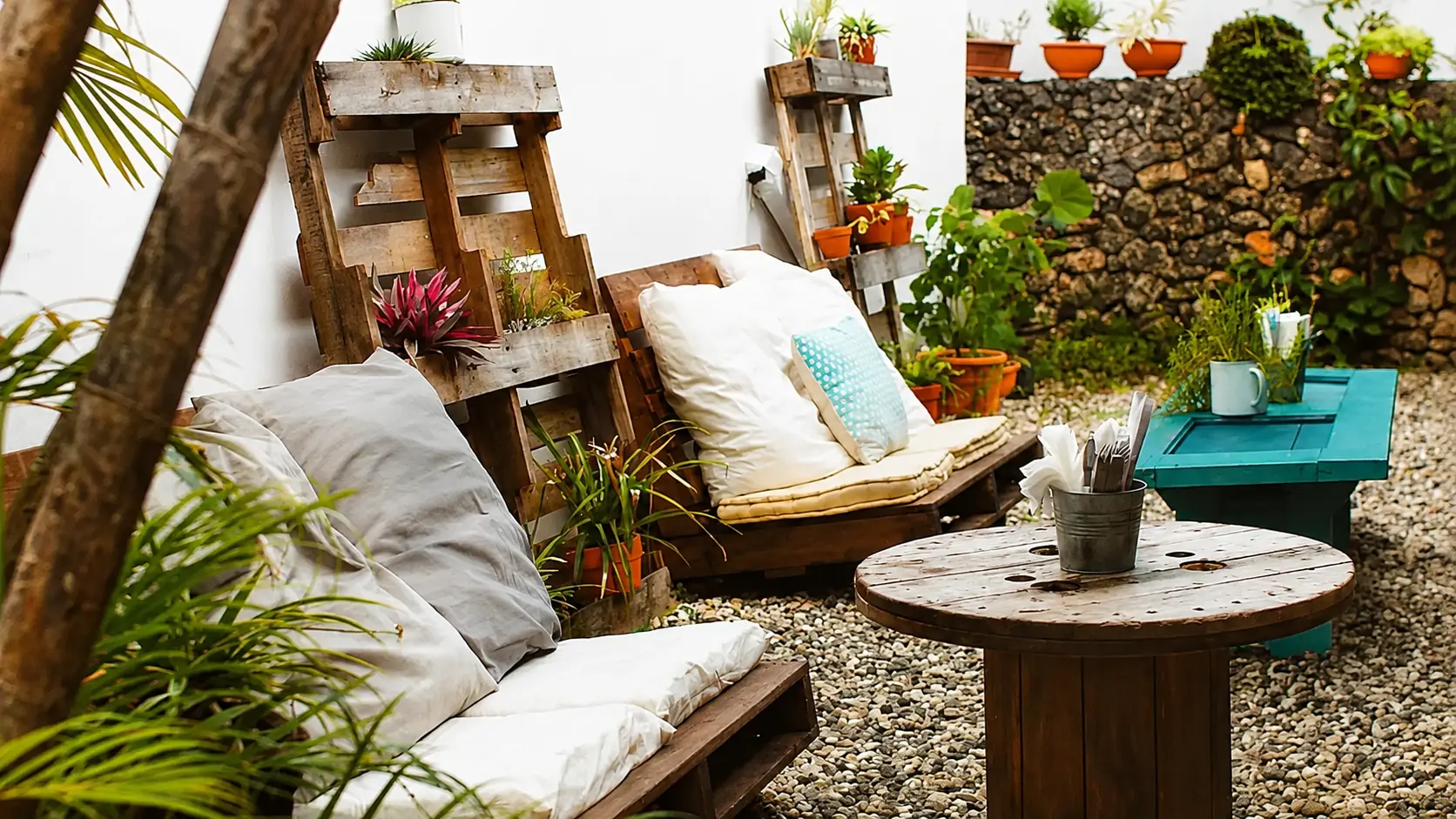 Leafy tropical courtyard lounge with rustic pallet furniture, potted plants and gravel floor